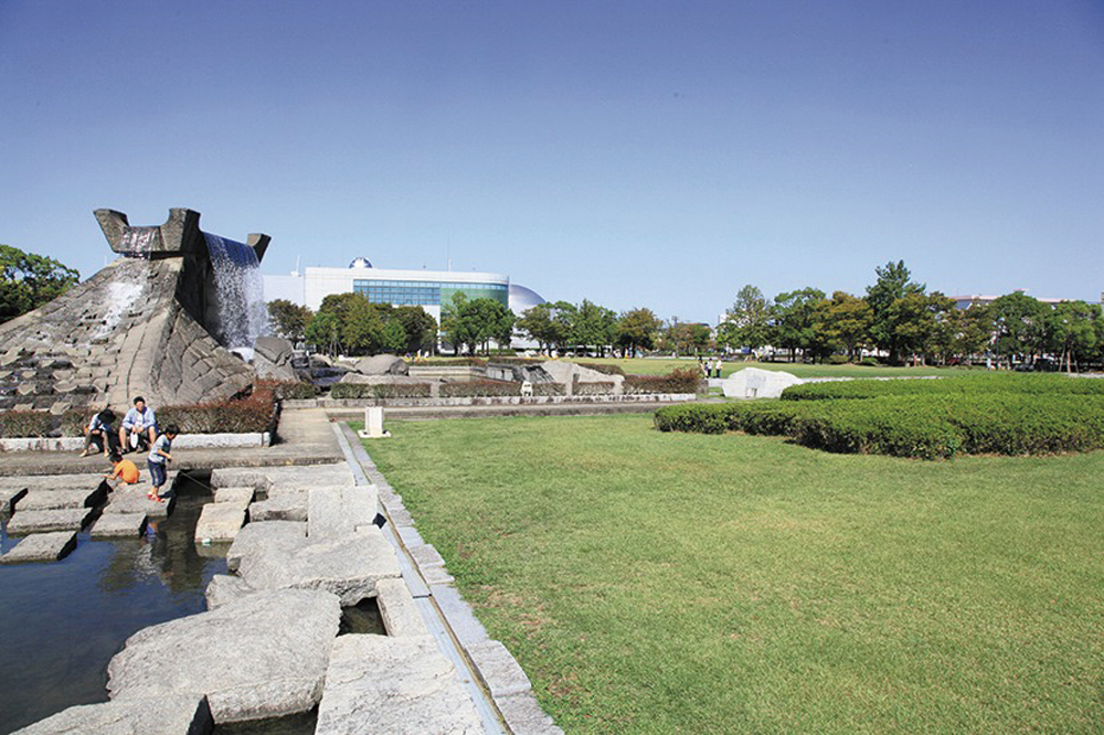 晴れた日の久留米市中央公園の、広い芝生広場と石造りの噴水