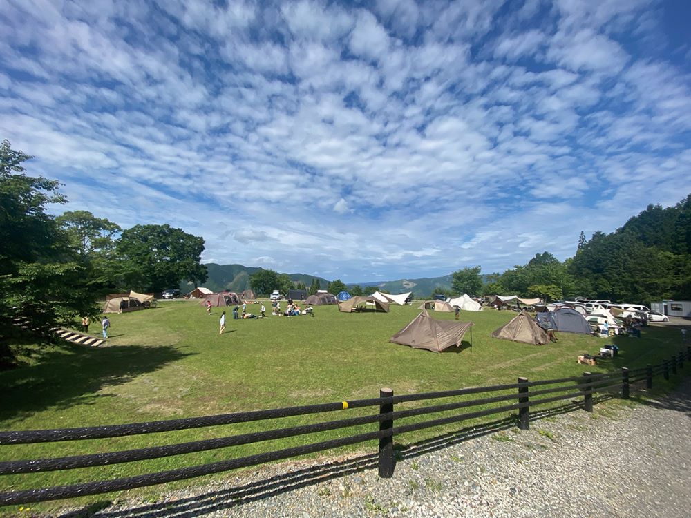 outsideBASE mizukamiの芝生広場で多くの人々がキャンプを楽しむ風景
