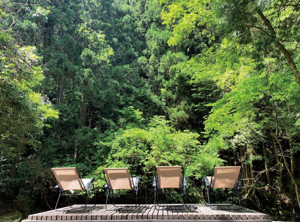 The Riverside Saunaの森に囲まれたウッドデッキとリクライニングチェア