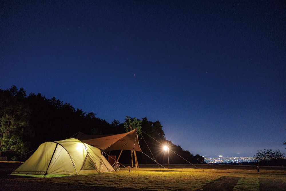 街の夜景を見下ろす高台で、星空の下ライトアップされたテント